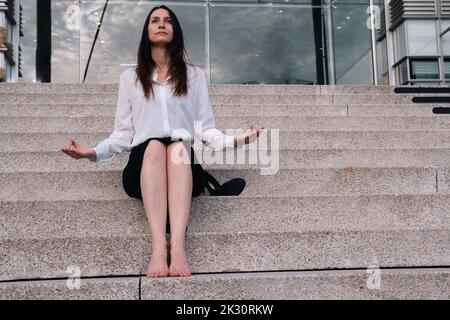 Nachdenkliche Geschäftsfrau, die Meditation auf Stufen macht Stockfoto
