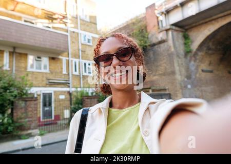 Lächelnde junge Frau mit Sonnenbrille und Selfie Stockfoto