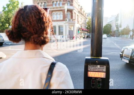 Frau wartet auf Fußgängerübergangstaste Stockfoto