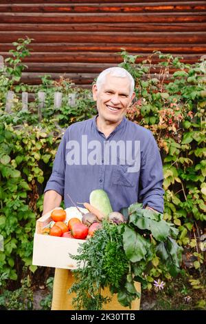 Glücklicher älterer Mann, der Gemüsekiste im Garten trägt Stockfoto