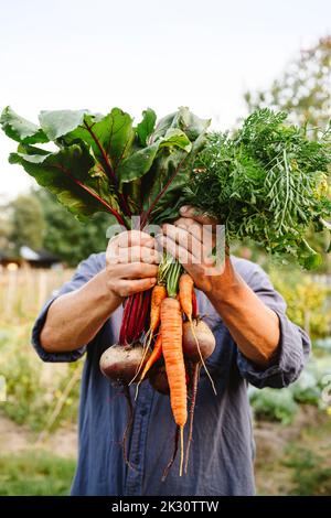 Mann versteckt Gesicht mit Gemüse im Garten Stockfoto