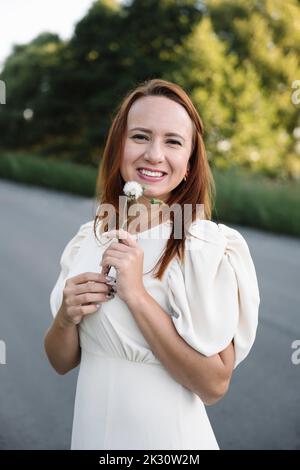 Lächelnde Frau in weißem Kleid mit weißer Blume auf der Straße Stockfoto