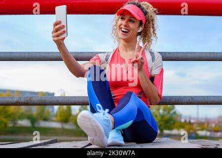 Glückliche Sportlerin beim Selfie auf dem Steg sitzend Stockfoto