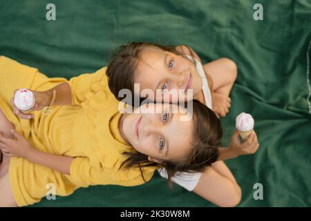 Lächelnde Geschwister mit Eiscreme, die sich auf der Decke von hinten auf den Rücken lehnen Stockfoto