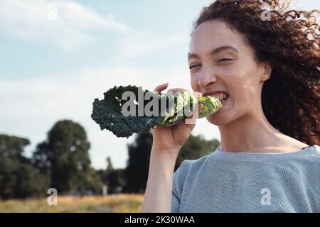 Frau mit lockigen Haaren beißt Grünblatt Stockfoto
