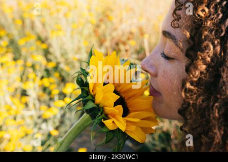 Junge Frau riecht gelbe Sonnenblume im Park Stockfoto