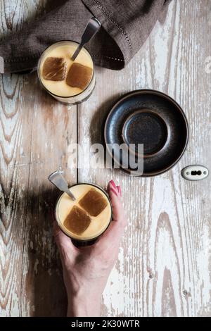 Hand einer Frau, die ein Glas veganen Eiskaffees mit Hafermilch aufhob Stockfoto
