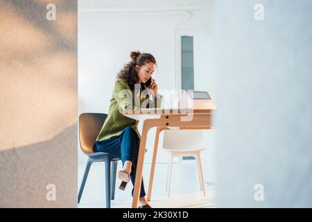 Geschäftsfrau, die mit dem Mobiltelefon spricht und am Schreibtisch sitzt und im Büro arbeitet Stockfoto