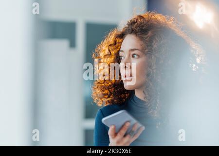 Nachdenkliche Frau mit lockigen Haaren und Smartphone Stockfoto