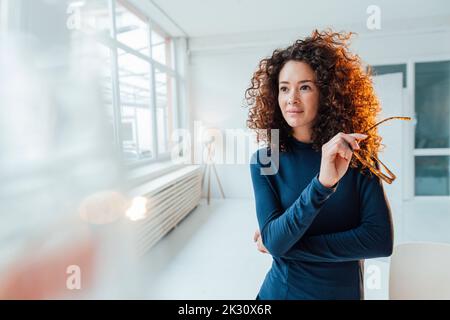 Eine durchdachte Geschäftsfrau mit lockigen Haaren und einer Brille Stockfoto