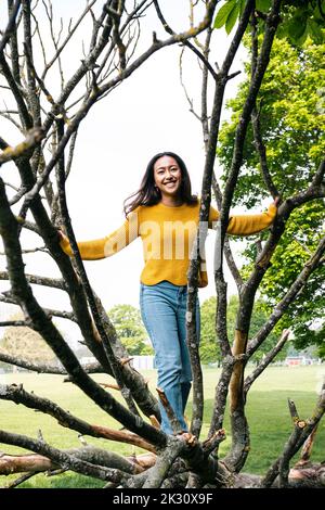 Glückliche junge Frau, die auf einem umgestürzten Baum im Park steht Stockfoto