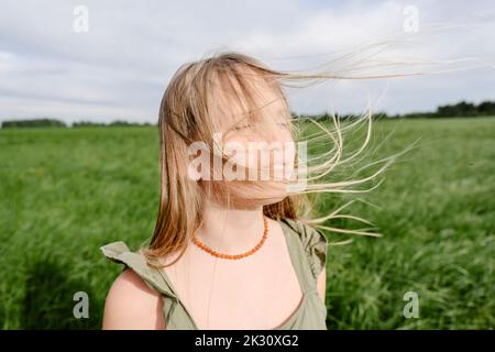 Mädchen mit blonden Haaren, die vom Wind auf dem Feld geblasen wurden Stockfoto