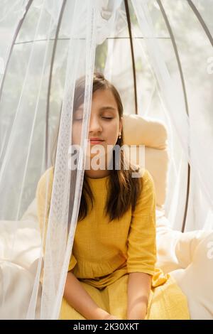 Vorpubertär Mädchen mit geschlossenen Augen sitzen in hängenden Stuhl Stockfoto