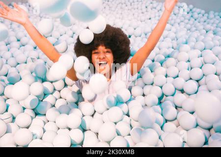 Verspielte junge Frau, die im Ballpool spielt Stockfoto