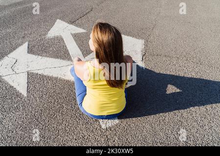 Frau sitzt auf drei-Wege-Pfeil-Zeichen Stockfoto