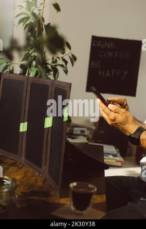 Geschäftsmann mit Smartphone lädt Tablet-PC mit Photovoltaik-Solarpanel Stockfoto