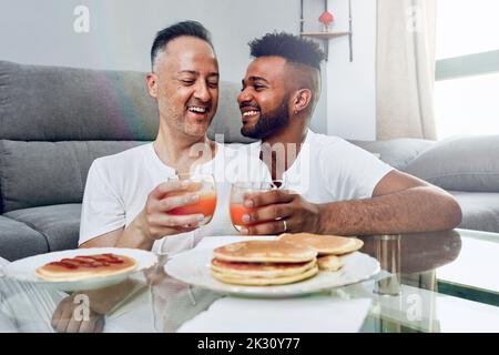 Glückliches schwules Paar, das zu Hause im Wohnzimmer gefrühstückt hat Stockfoto