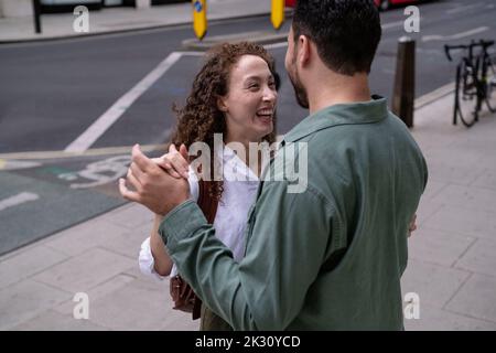 Fröhliche junge Frau mit Mann, der auf dem Fußweg tanzt Stockfoto