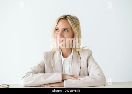 Lächelnde Geschäftsfrau, die am Schreibtisch sitzt und wegschaut Stockfoto
