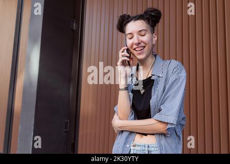 Glückliche, nicht-binäre Person, die auf dem Smartphone spricht Stockfoto