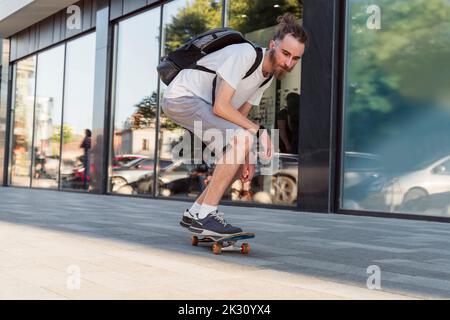 Junger Mann mit Rucksack Skateboarding auf Fußpfad Stockfoto