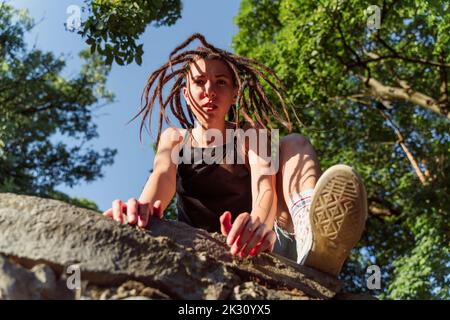 Junge nicht-binäre Person, die auf einer Steinwand klettert Stockfoto