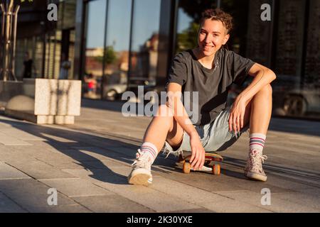 Lächelnde nicht-binäre Person, die auf dem Skateboard sitzt Stockfoto