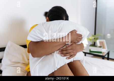 Verärgert Frau versteckt Gesicht in Kissen, während auf dem Bett sitzen Stockfoto