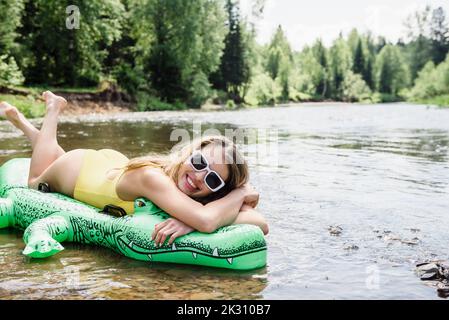 Frau liegt auf aufblasbarem Krokodil im Fluss Stockfoto