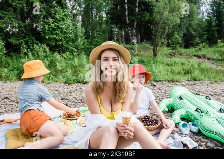 Lächelnde Frau hält Eis und sitzt mit Söhnen auf dem Picknick Stockfoto