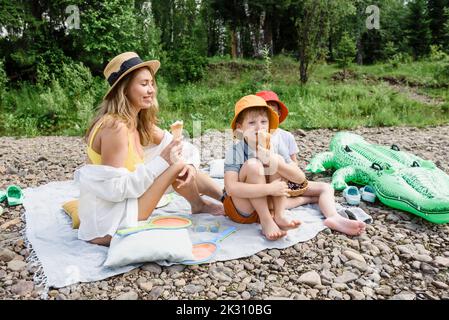 Frau, die Eis isst, und Söhne, die auf einer Picknickdecke sitzen Stockfoto