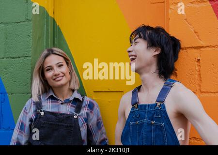 Junge Freunde, die mit einander vor dem Regenbogen an der Wand stehen Stockfoto