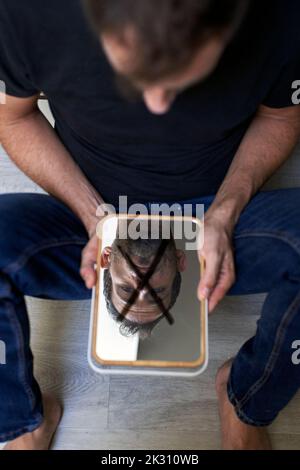 Trauriger Mann, der Spiegel mit Kreuzmarkierung hält Stockfoto