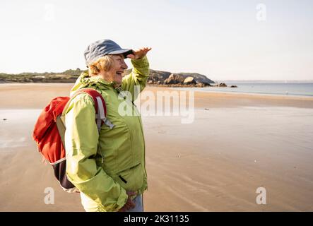 Glückliche ältere Frau, die die Augen am Strand abschirmt Stockfoto