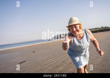 Glückliche ältere Frau, die am Strand Daumen nach oben zeigt Stockfoto