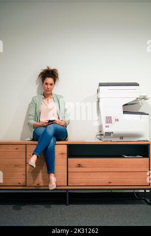 Selbstbewusste Geschäftsfrau, die im Büro auf einem Aufbewahrungsschrank sitzt Stockfoto