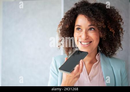 Lächelnde Geschäftsfrau, die Voicemail über das Smartphone sendet Stockfoto