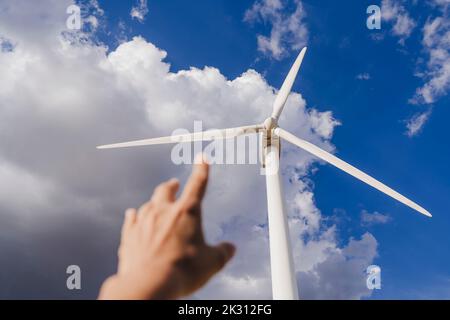 Hand einer Frau, die unter Wolken am Himmel auf den Rotor der Windenergieanlage gestikuliert Stockfoto