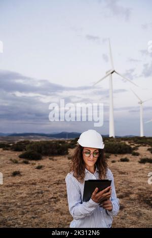Techniker mit Hardhut am Tablet-PC im Windpark Stockfoto