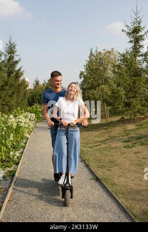 Junge Frau mit Freund genießen Elektroroller Fahrt im Park Stockfoto