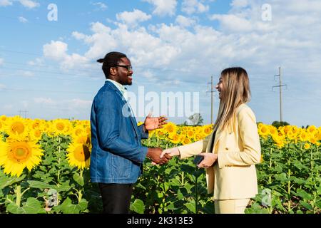 Glückliche Geschäftsfrau schüttelt sich die Hände mit Geschäftsmann in Sonnenblumenfeld Stockfoto