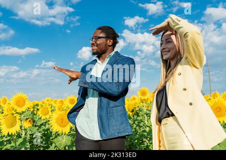 Glücklicher junger Geschäftsmann, der mit Geschäftsfrau vor Sonnenblumenpflanzen diskutiert Stockfoto