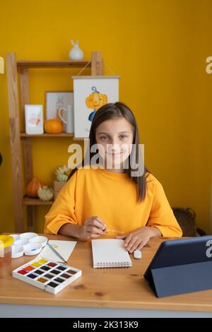 Lächelndes Mädchen mit Skizzenblock am Tisch sitzend Stockfoto