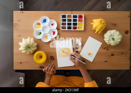 Mädchen mit Aquarellen, die Jack O' Lantern auf einem Skizzenblock am Tisch malen Stockfoto