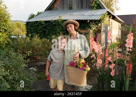 Lächelnde ältere Frau mit Hut und Enkel vor dem Haus Stockfoto