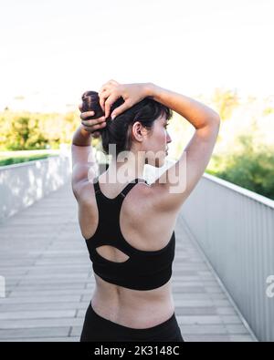 Junge Frau, die das Haar justiert, steht auf der Brücke Stockfoto