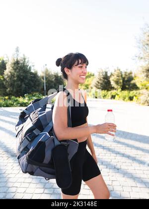 Fröhliche junge Sportlerin mit Sporttasche, die auf dem Fußweg läuft Stockfoto