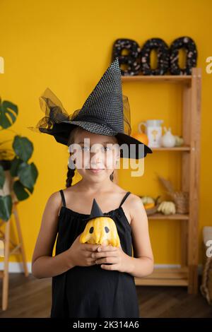 Lächelndes Mädchen mit Hexenkostüm, das Kürbis zu Hause hält Stockfoto