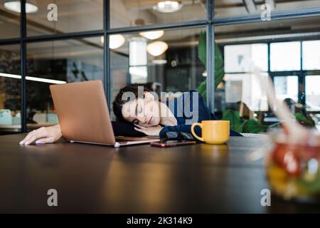 Müde Geschäftsfrau mit Laptop, die im Büro ein Nickerchen macht Stockfoto
