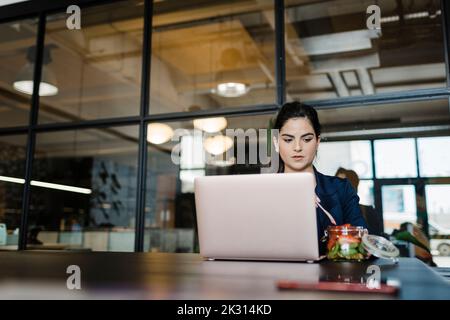 Junge Frau mit Obst am Laptop im Büro Stockfoto